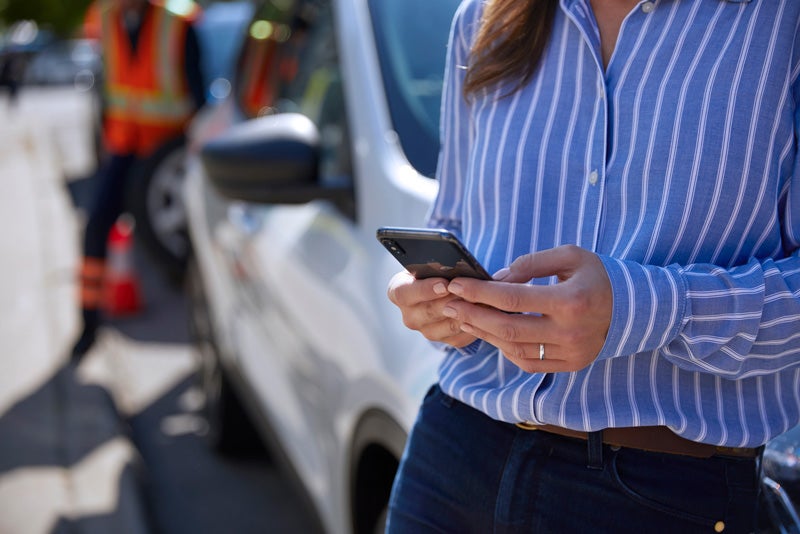 A women using her phone with a Mustang Mach-E in the background