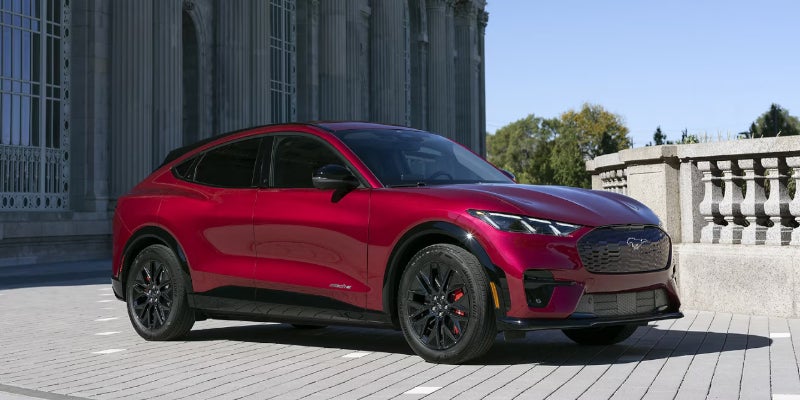 A red 2025 Mustang Mach-E in front of a posh building